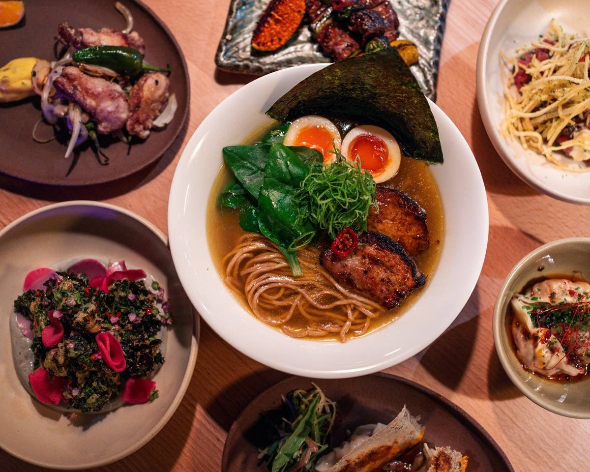 a bowl of ramen surrounded by a variety of side dishes and small plates