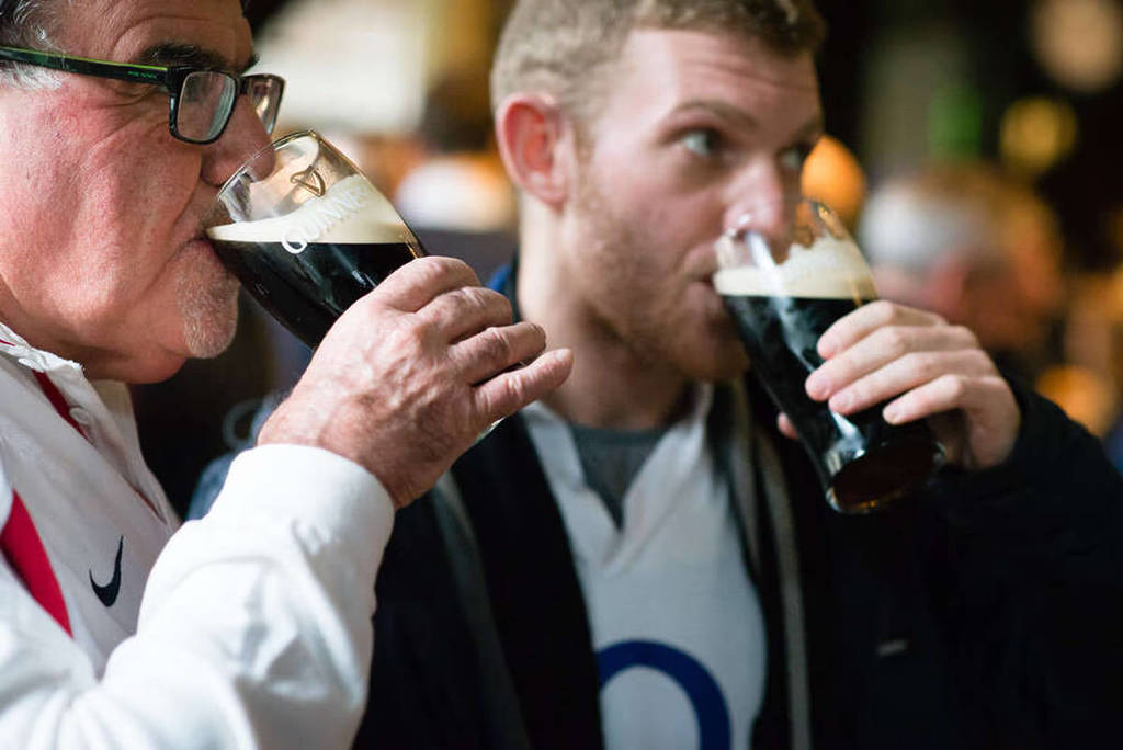 two men sipping on pints of guinness in a pub while they watch the six nations