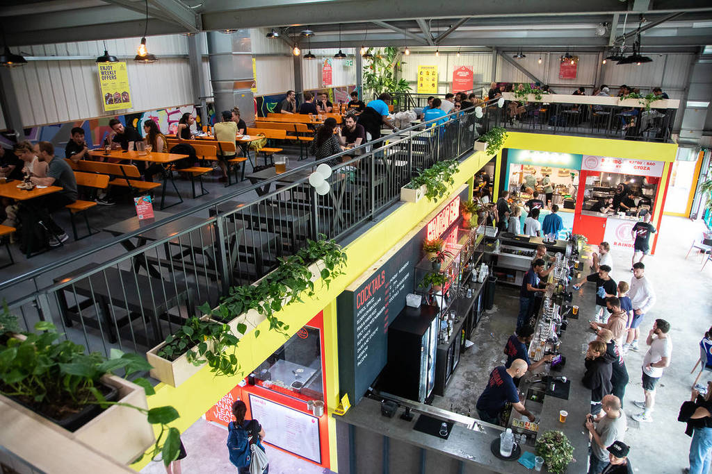a multi-level indoor food and drink market with stalls downstairs and tables and seating upstairs