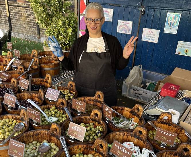 Person behind a stall selling olives at a Farmers Market