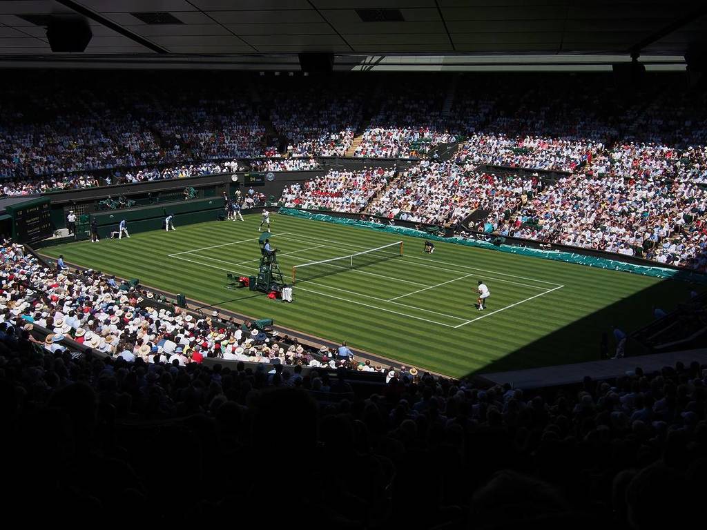 Auf dem Centre Court in Wimbledon sehen wir ein Einzelspiel, das auf dem üppigen grünen Rasen und bei vollen Plätzen auf dem Platz ausgetragen wird.
