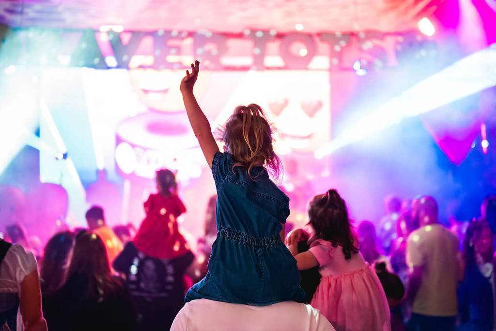 Raver tots festival stage child on parent's shoulder