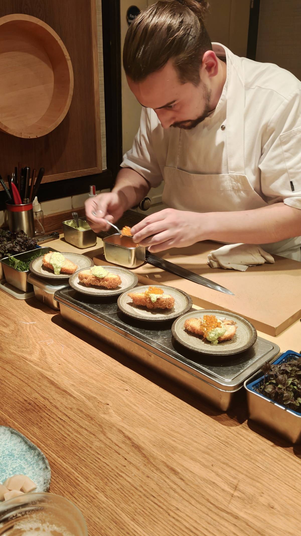 a sushi chef at niju hard at work putting the final touches to four plates of fish katsu in an 'at the counter' omakase experience