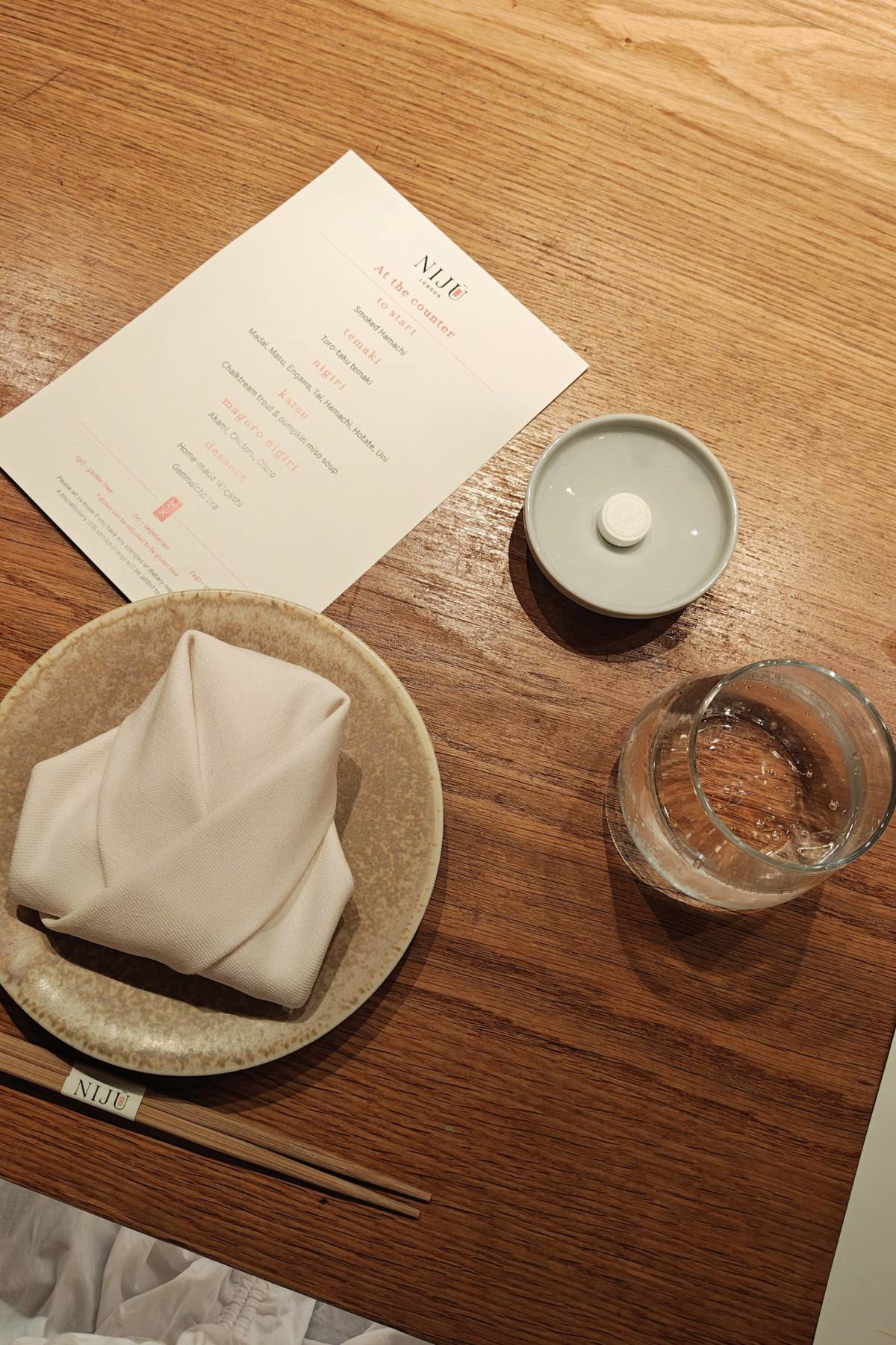 a table setting with a napkin folded like a robe, a glass of water, and a menu