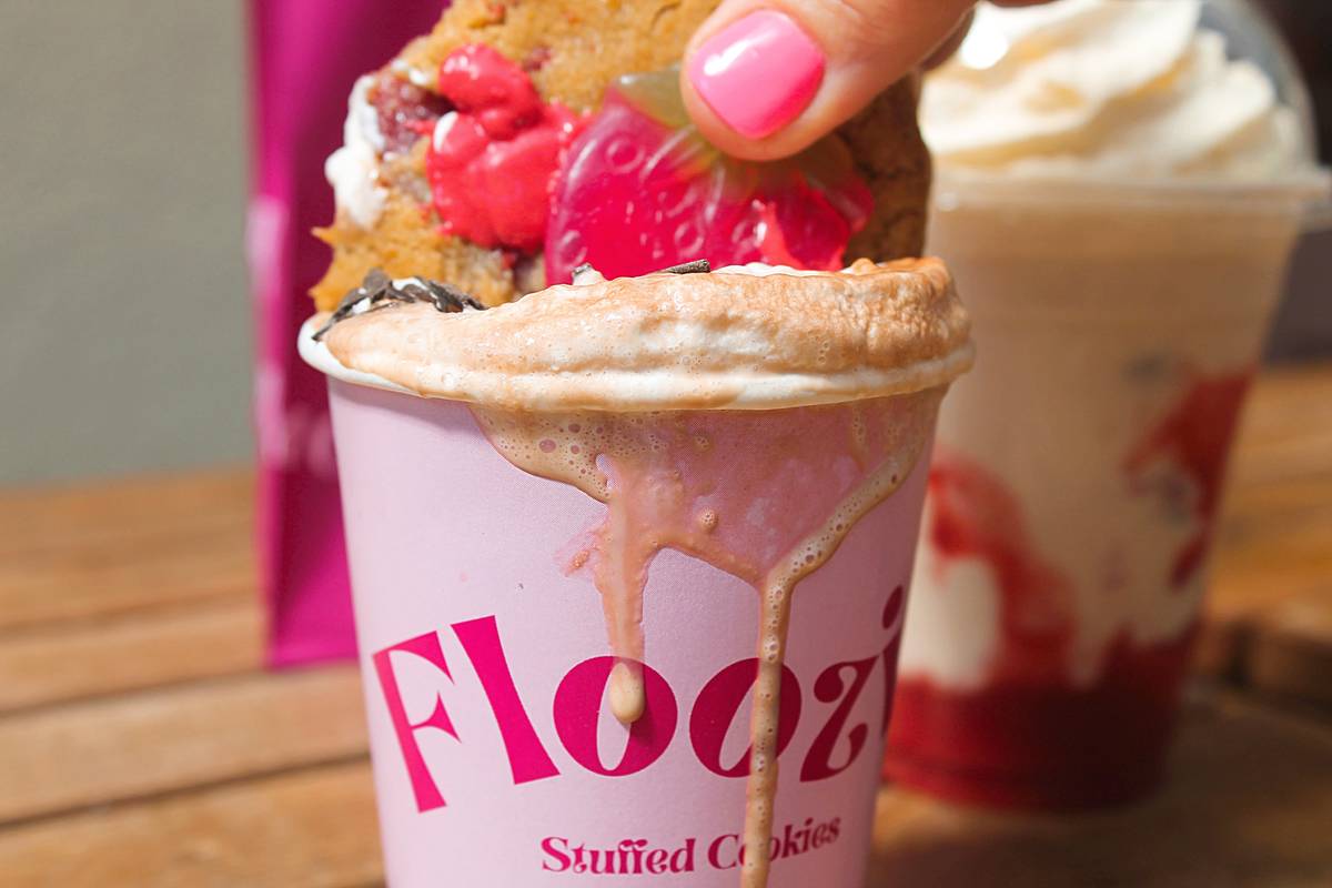 a cookie being dunked into a decadent looking hot drink in a floozie branded cup