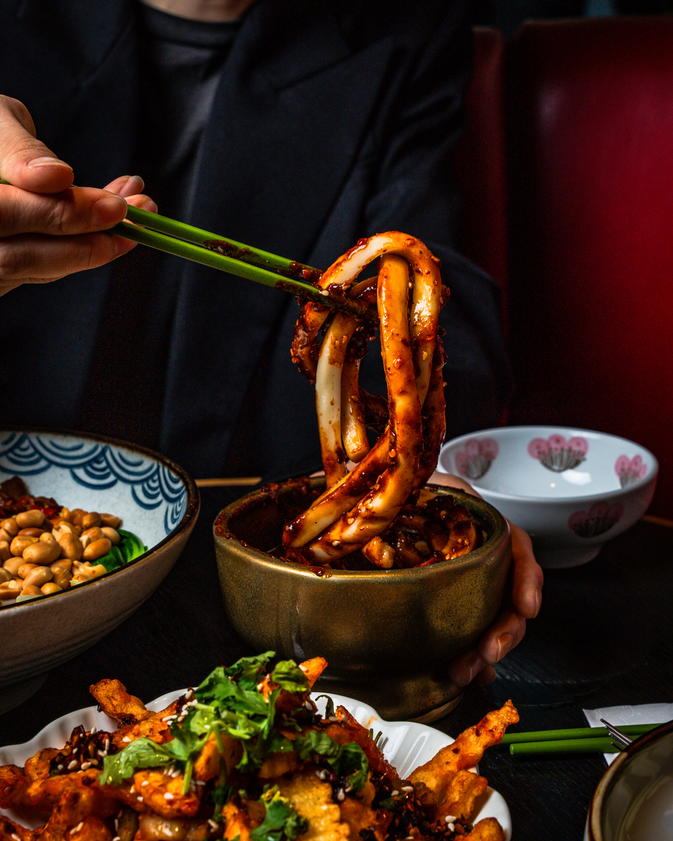 a slippery saucy portion of noodles being grabbed by a pair of chopsticks