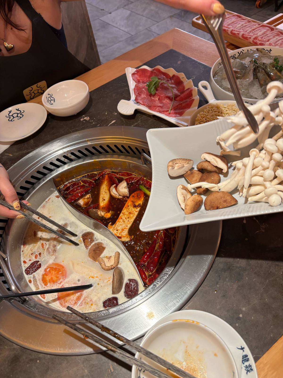 mushrooms being placed into a pot of boiling soup that is split into two different flavours