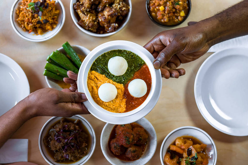 Un colorido cuenco de comida que se pasa de mano en mano sobre una mesa cubierta de comida nigeriana.