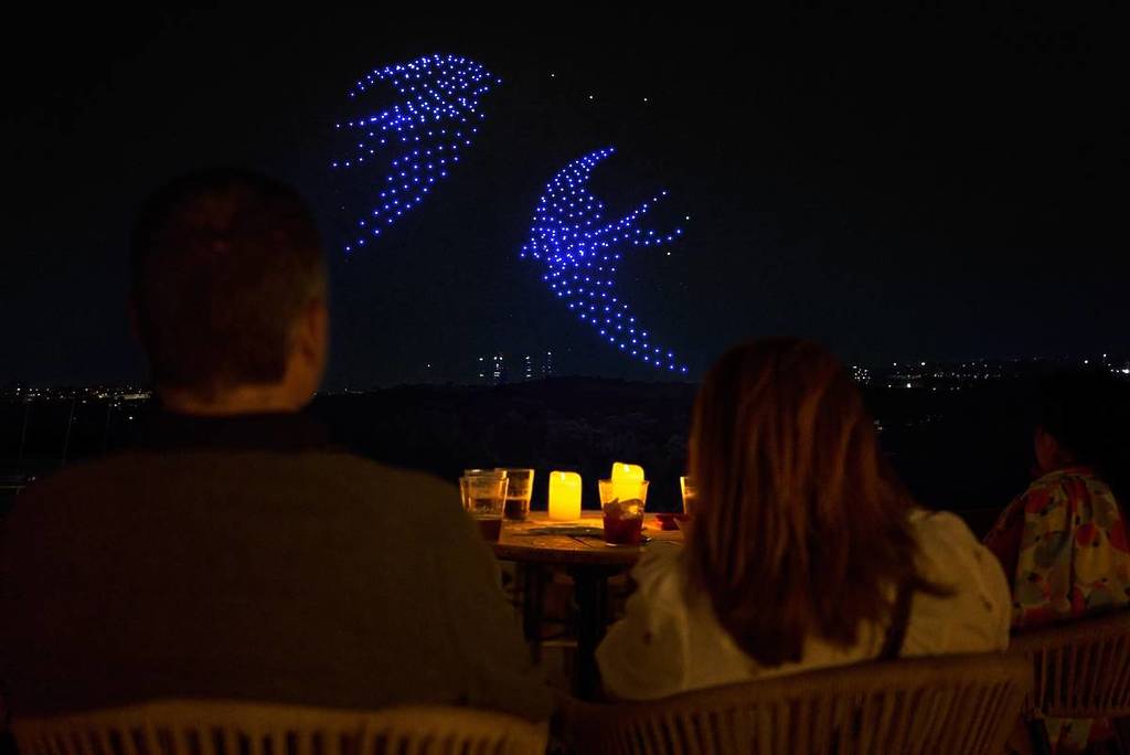 a couple watch a drone art show depicting flying swallows