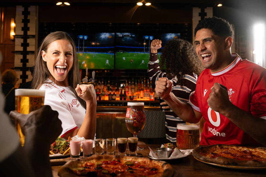 fans cheering around a table covered in food and drinks as the six nations plays on tv behind them