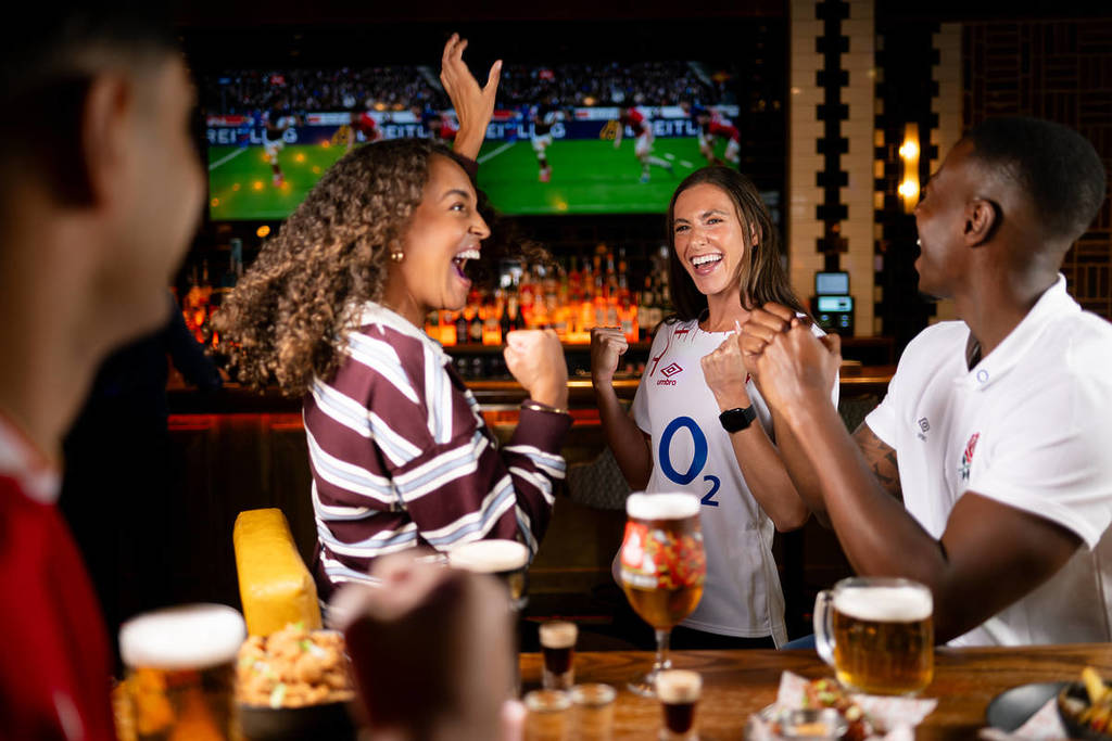 fans cheering around a table covered in food and drinks as the six nations plays on tv behind them