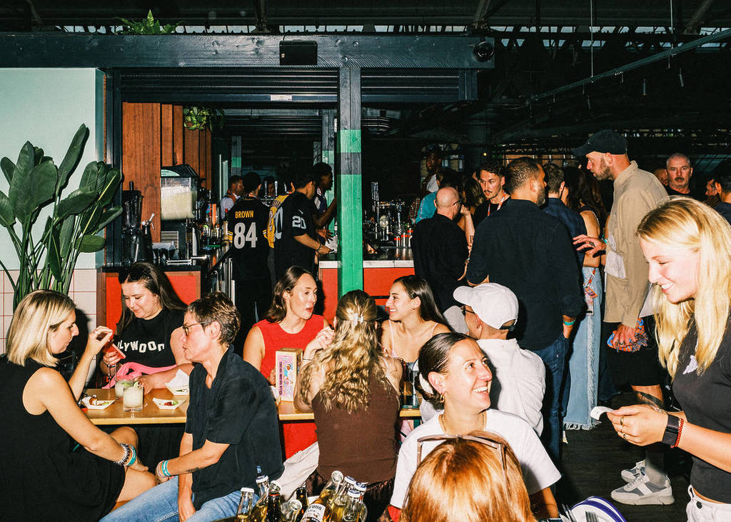 a room full of people sat down at tables and standing around enjoying drinks and food