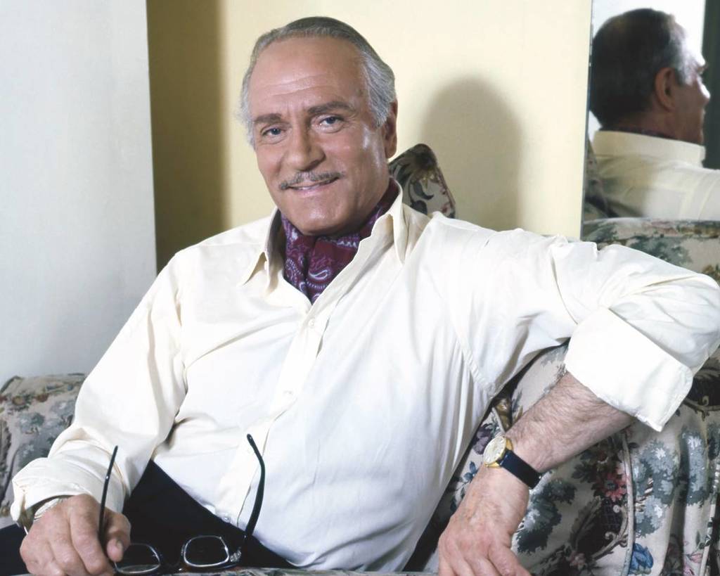 A portrait of Laurence Olivier sat down, holding his glasses