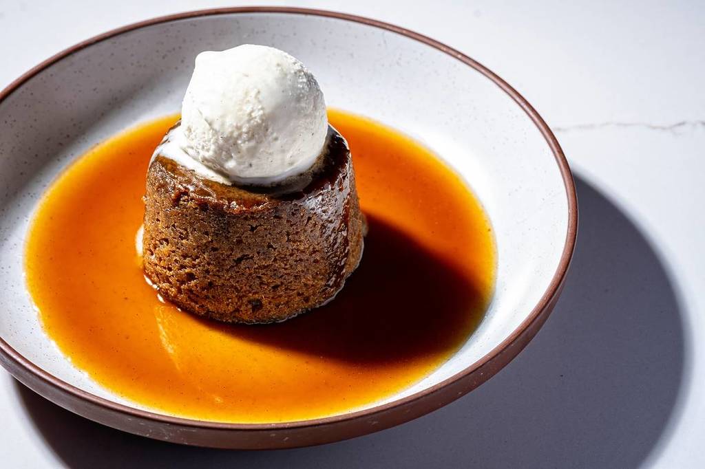 um pudim de caramelo pegajoso sobre uma poça de caramelo, com uma bola de gelado por cima