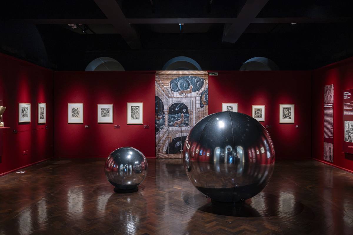 Exhibition space at M.C. Escher: The Exhibition, featuring famous prints and metalic orbs.