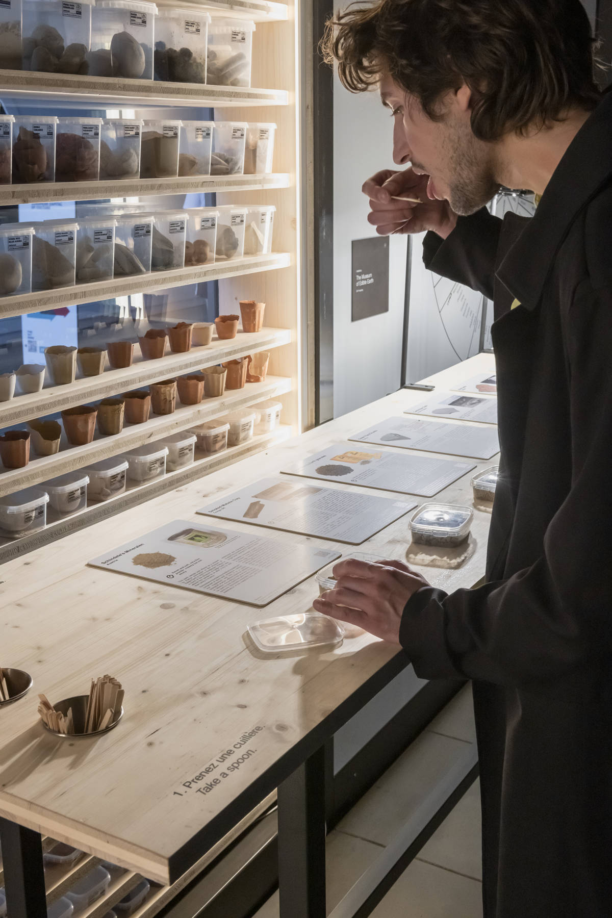 someone sampling a bit of earth at the museum of edible earth, while reading a description of the tasting notes and history of the sample