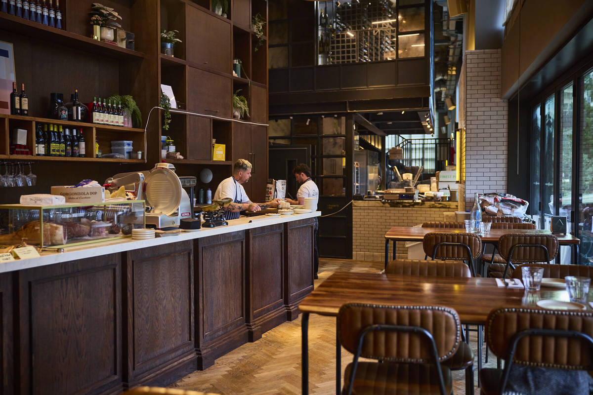the interior of bar brasso restaaurant and feli showing people woking behind a long wooden counter with tables and chairs visible on the other side for customers