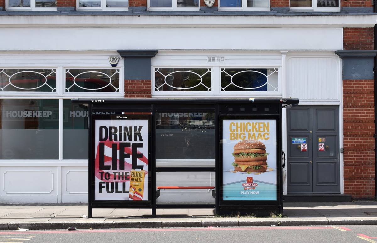 London, UK - Oct 01, 2025: Empty London bus stop featuring McDonald’s and healthy drink advertisements, with a historic building in the background on a sunny day
