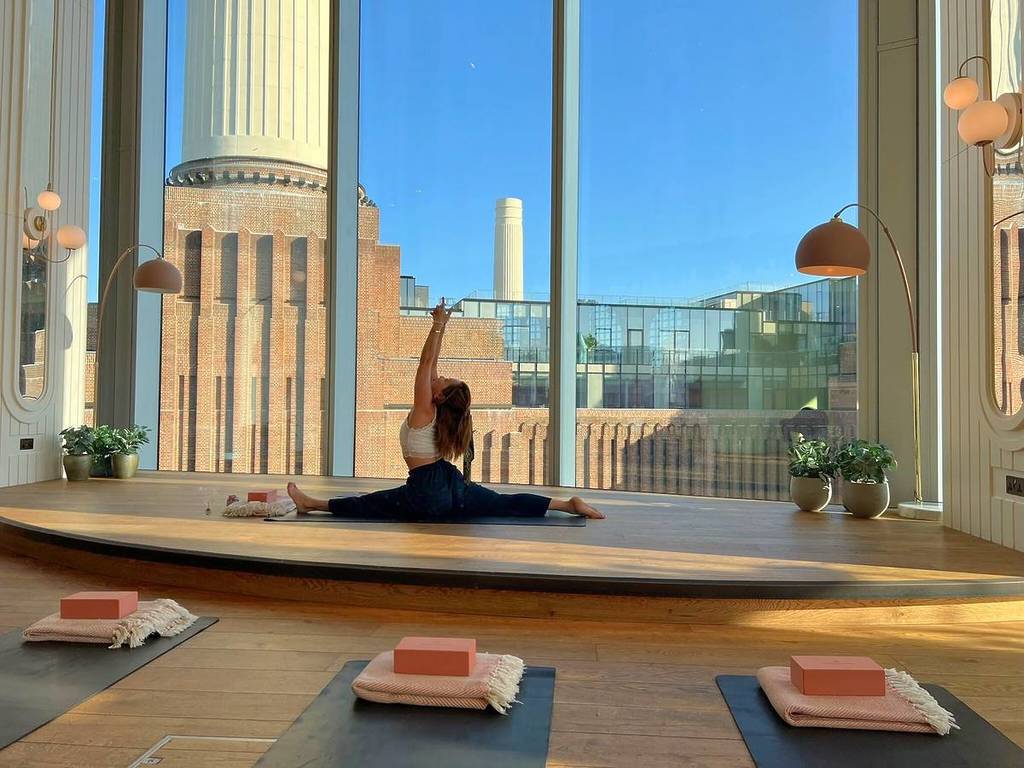 Una mujer hace una postura de yoga frente a una ventana gigante desde la que se puede ver la central eléctrica de Battersea.