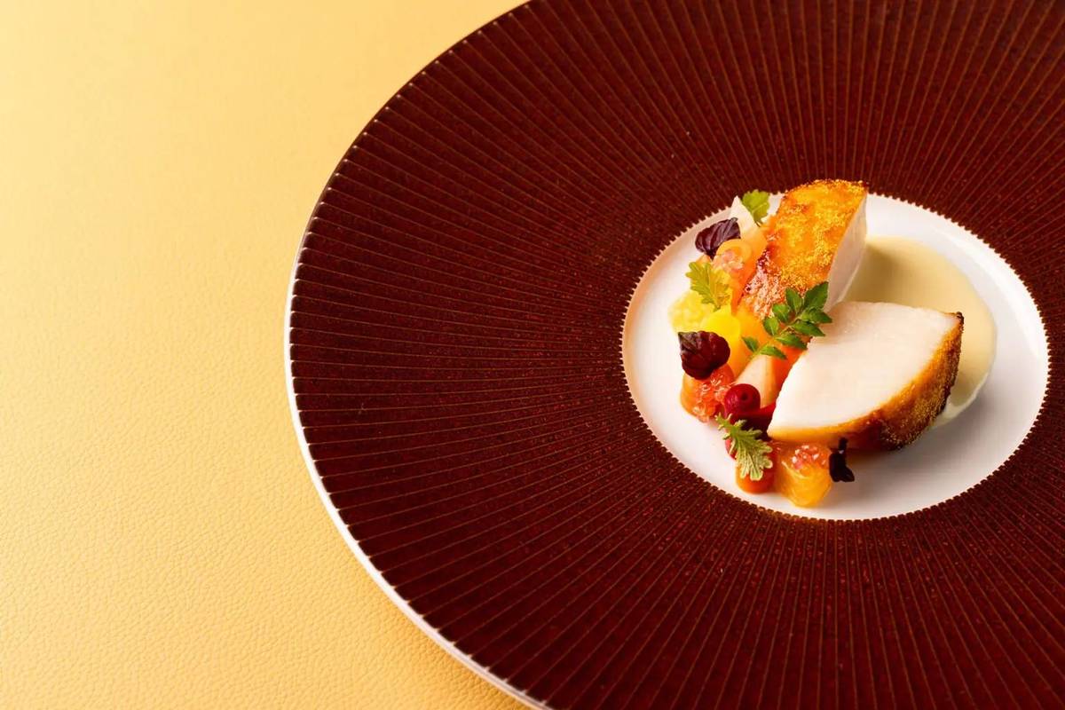 a large plate with a fancily small portion of food in the centre, displayed against a yellow backdrop