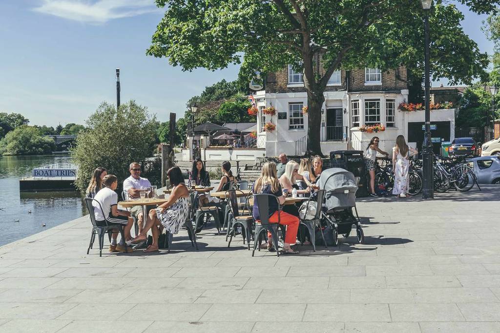 La gente se sentaba en los bancos fuera de un pub en un día soleado junto al río