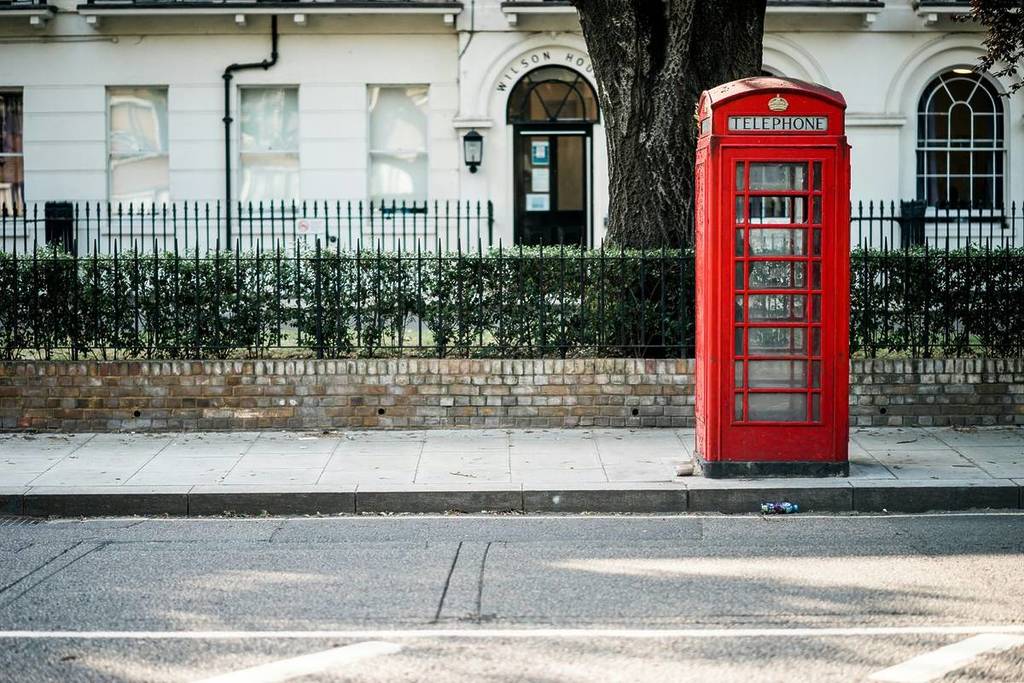 Eine Londoner Straße mit einem weißen Haus hinter einer Hecke und einem schwarzen Tor mit einer roten Telefonzelle draußen