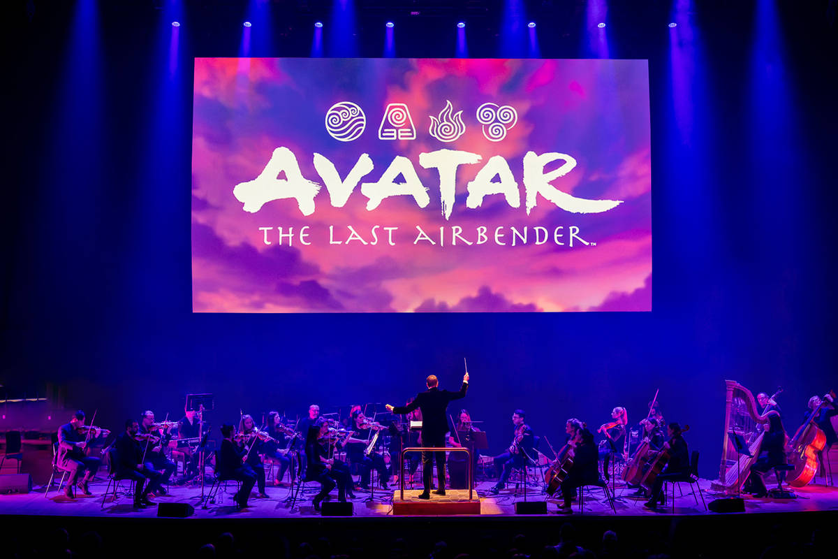 a live orchestra on stage under a screen with a shot of the title card for 'avatar the last airbender'