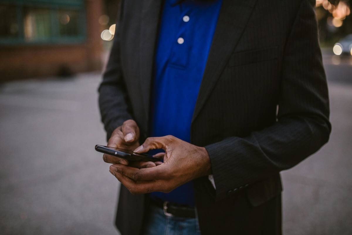 a man in a blue polo and black jacket typing on his phone