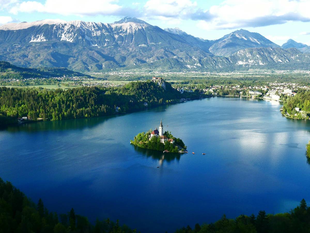 A bright blue lake with a small green island in the centre. In the background you snowy mountains are visible.