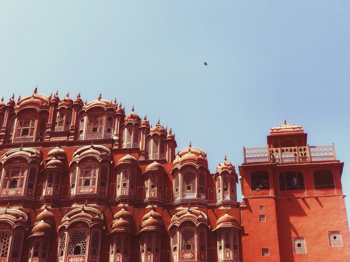 A corner of a terracotta building with intricate design on it is shot from below with the blue sky behind it