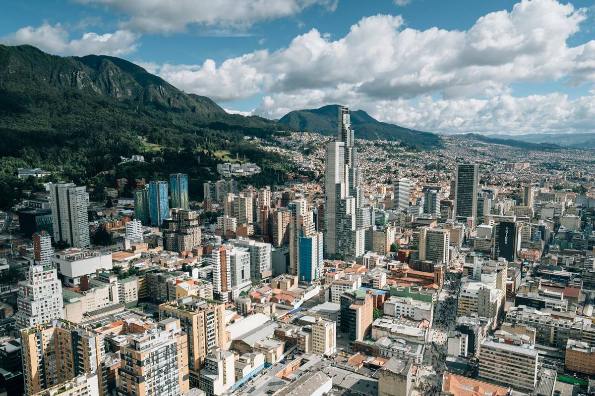 A sprawling city with some high skyscrapers with a green mountain range in the background.