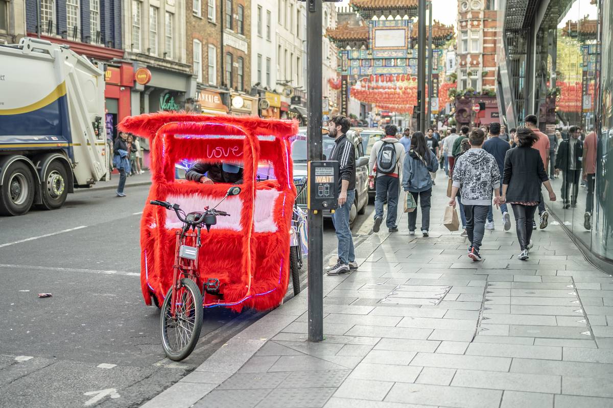 A red and fluffy pedicab parked up next to a pavement in London