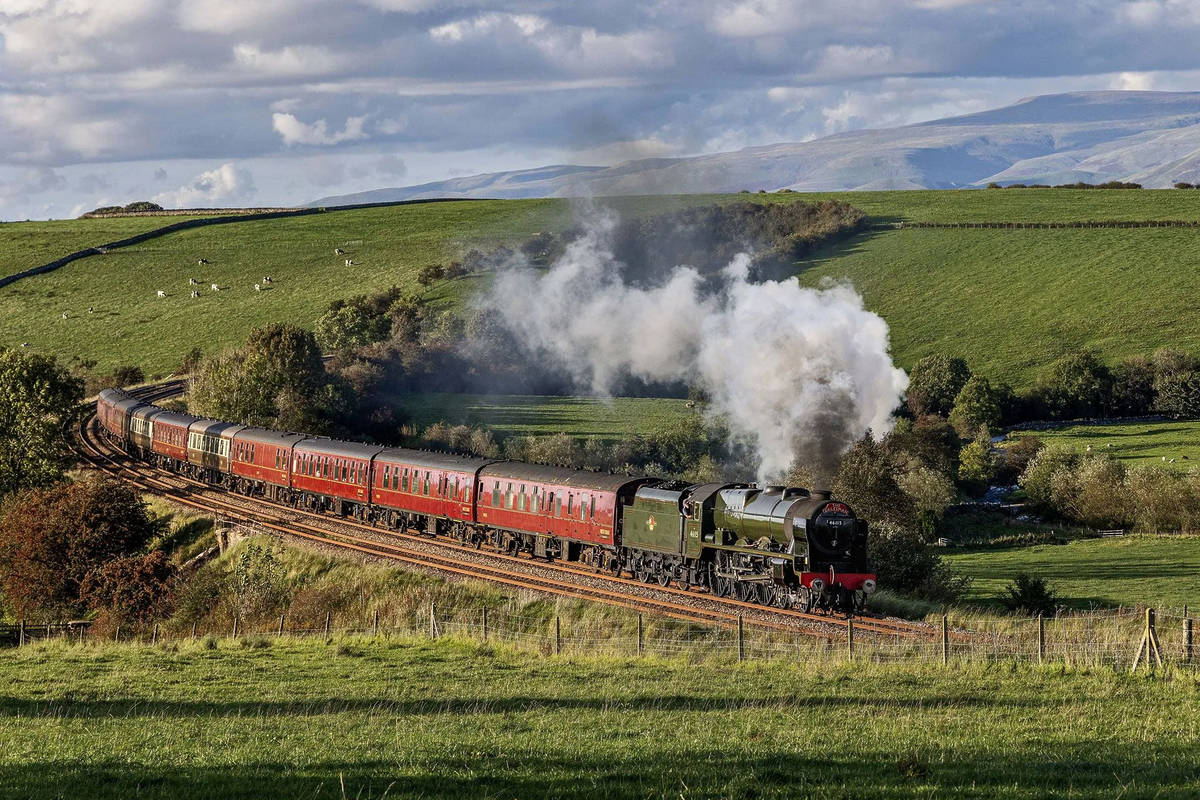 The cumbrian mountain express steam train journey winding its way through a verdant landscape, with steam billowing out of the train