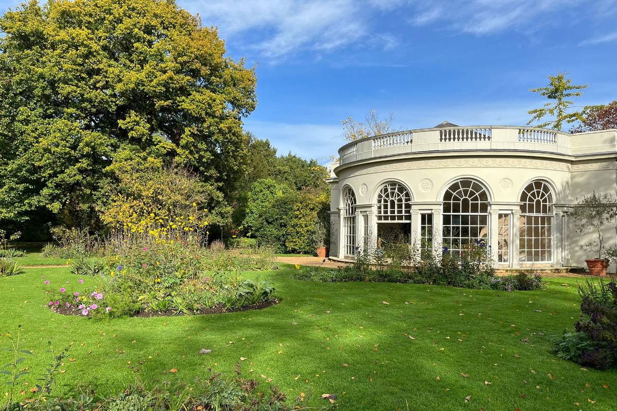 Een keurig onderhouden tuin met een groen gazon, planten verspreid over het gazon en een rond wit gebouw met boogramen.