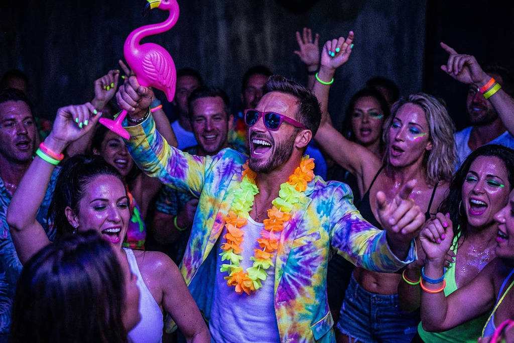 Um grupo de pessoas a rir e a dançar no Mingo Bingo, enquanto um homem com acessórios de néon segura um flamingo