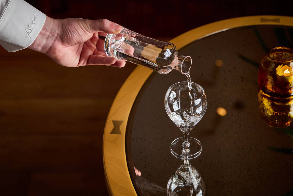 sake being poured from a glass bottle into a glass atop a table