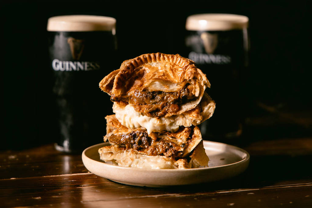 a pie that has been cut in half and stacked, cut side facing out, to expose the fillings, with two pints of Guinness in the background