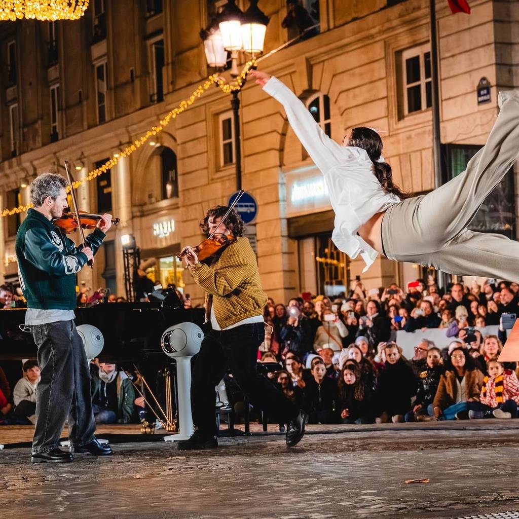 a violin dup performing in the streets of paris, surrounded by an audience, with a dancer flinging themself into the air in the foreground