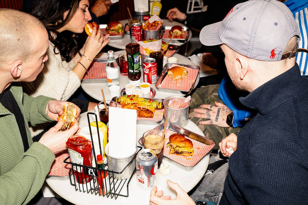 a group of people sat around  table eating burgers and chips