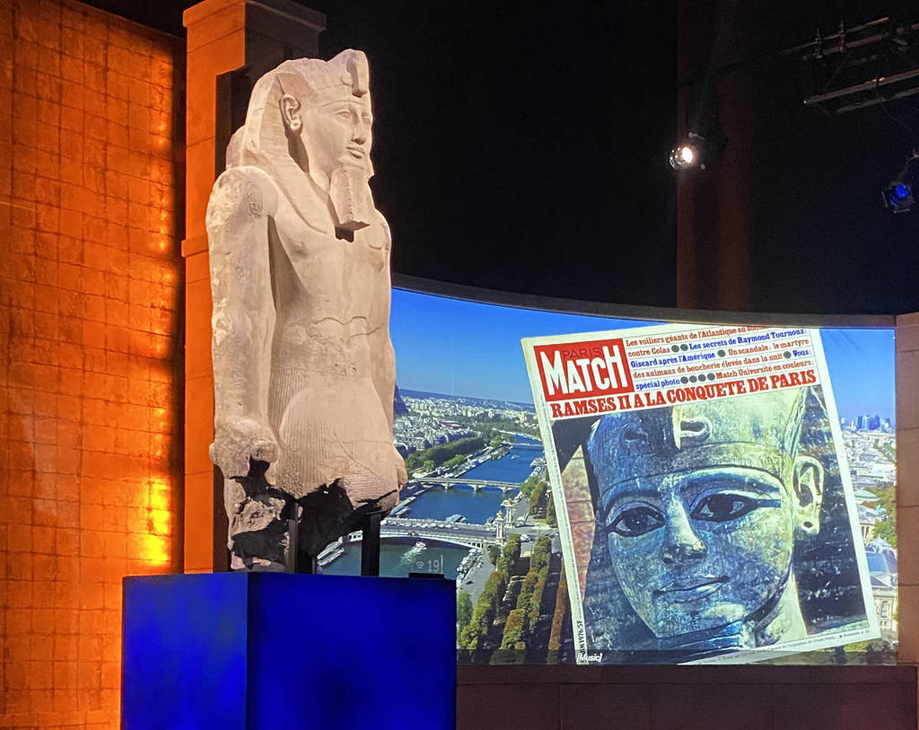 Ein Kalksteinkoloss von Ramses II. mit einem Bildschirm, der eine französische Zeitung dahinter zeigt, in der Ausstellung „Ramses und das Gold der Pharaonen“.