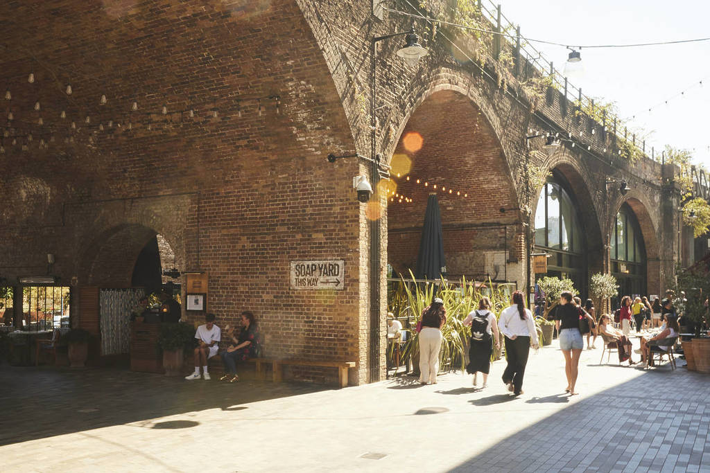people walking past archways in the sun at borough yards