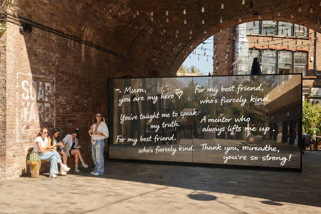 Menschen stehen und sitzen neben einer Spiegelwand, die mit Botschaften der Liebe und Wertschätzung bedeckt ist