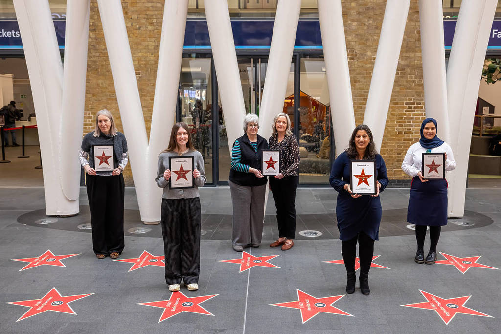 Eine Gruppe von Frauen steht herum und hält gerahmte Sterne in der Hand, über Sternen auf dem Boden auf einer Spur von Sternen, die Frauen in Schienen feiern