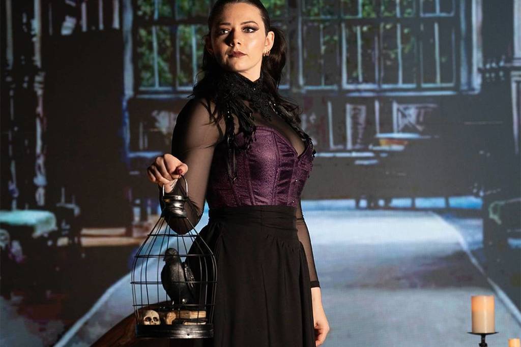 Eine Frau in gotischer Kleidung hält einen Raben in einem Käfig im Edgar Allan Poe Speakeasy.