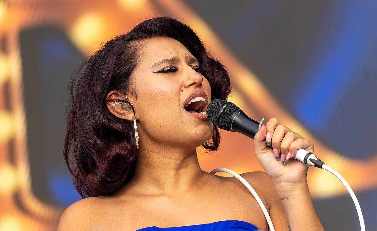 Raye singing into a microphone wearing a blue outfit