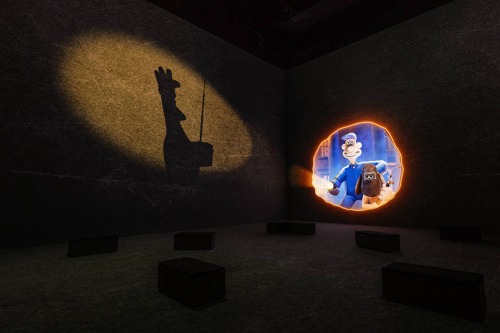uma imagem estática de um filme de Wallace e Gromit projetada nas paredes, com a silhueta sombria de um pinguim malvado visível no feixe de luz de uma lanterna
