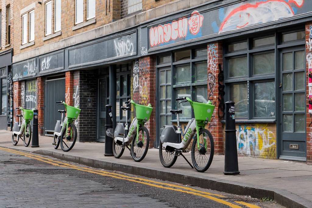 Una fila de bicicletas Lime aparcadas frente a una pared con grafitis en Londres.