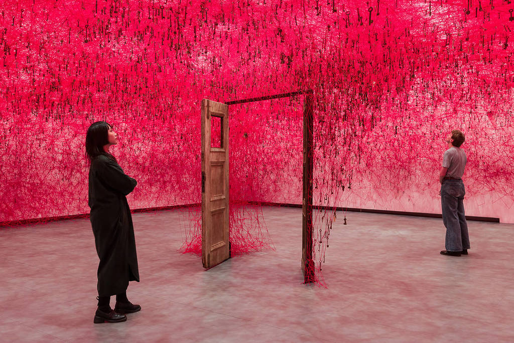 Menschen standen um eine offene Tür in einem raumfüllenden Fadenmassen, die durch den ganzen Raum huschten und eine wolkenverhangene Fadenmasse in der Luft bildeten, gefüllt mit Hunderten von hängenden Schlüsseln