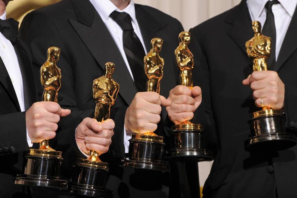 3 Männer in Anzügen halten 5 goldene Oscar-Auszeichnungen vor sich