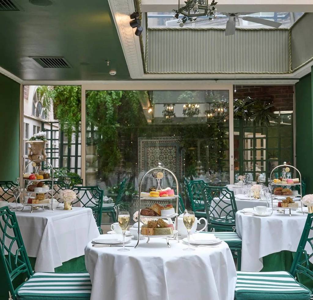 uma sala arejada com mesas de linho branco adornadas com tabuleiros de chá da tarde em camadas